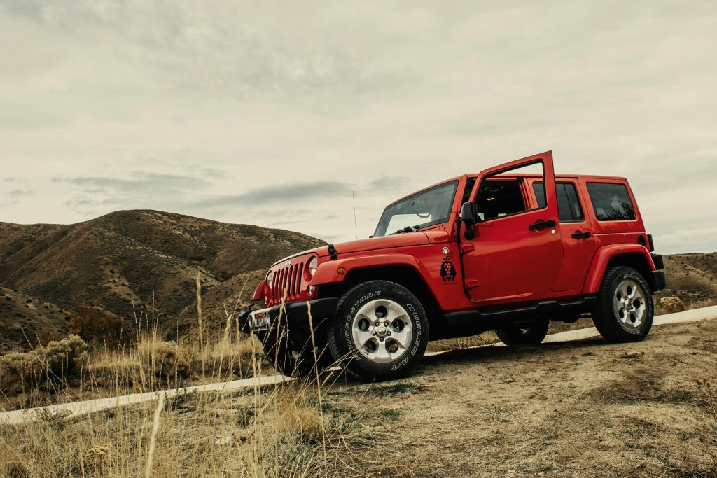 A vibrant red SUV parked on a dirt road with a mountain landscape backdrop under a cloudy sky.